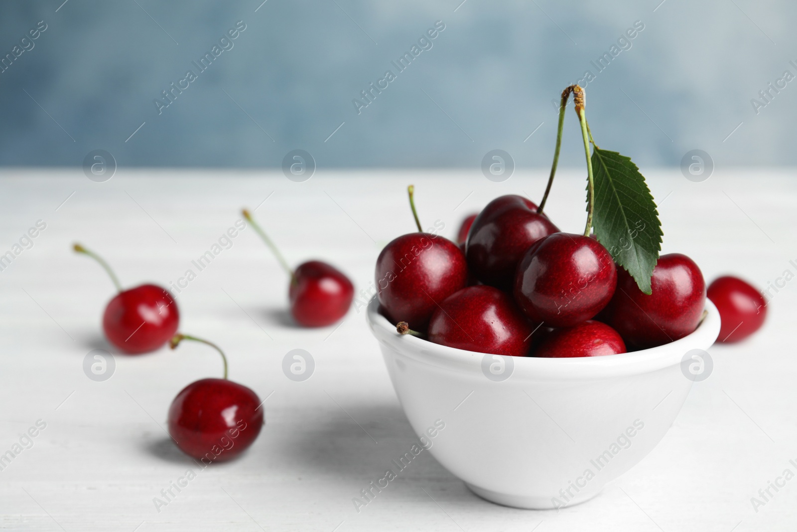 Photo of Bowl with sweet cherries on white wooden table. Space for text