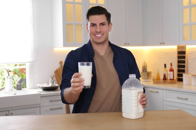 Photo of Man with glass and gallon bottle of milk at wooden table in kitchen