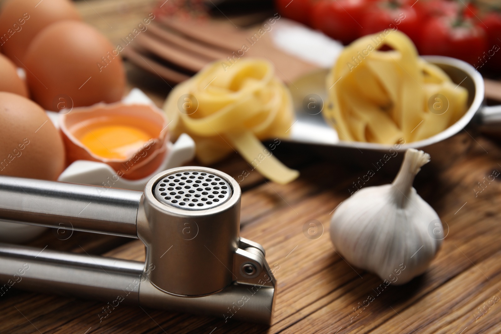 Photo of Fresh garlic and press on wooden table, closeup. Cooking utensil