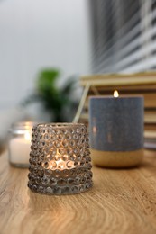 Lit candles in different holders on wooden table indoors. Space for text