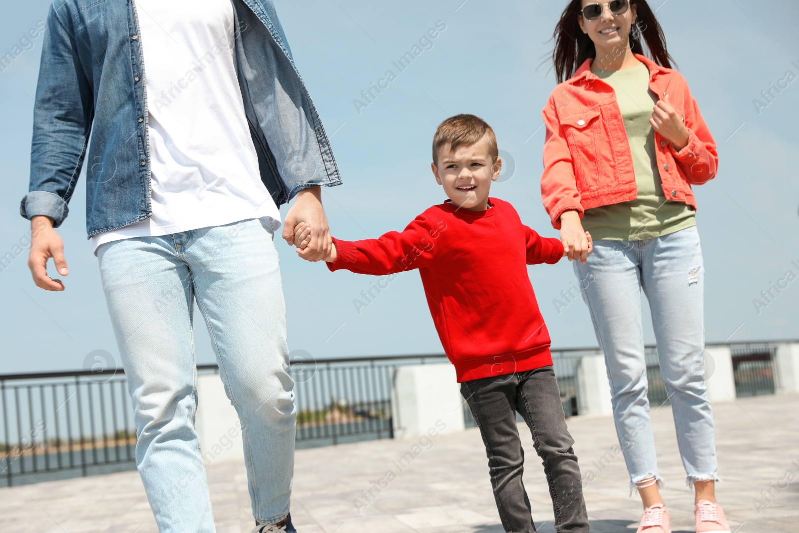 Photo of Happy child holding hands with his parents outdoors. Family weekend