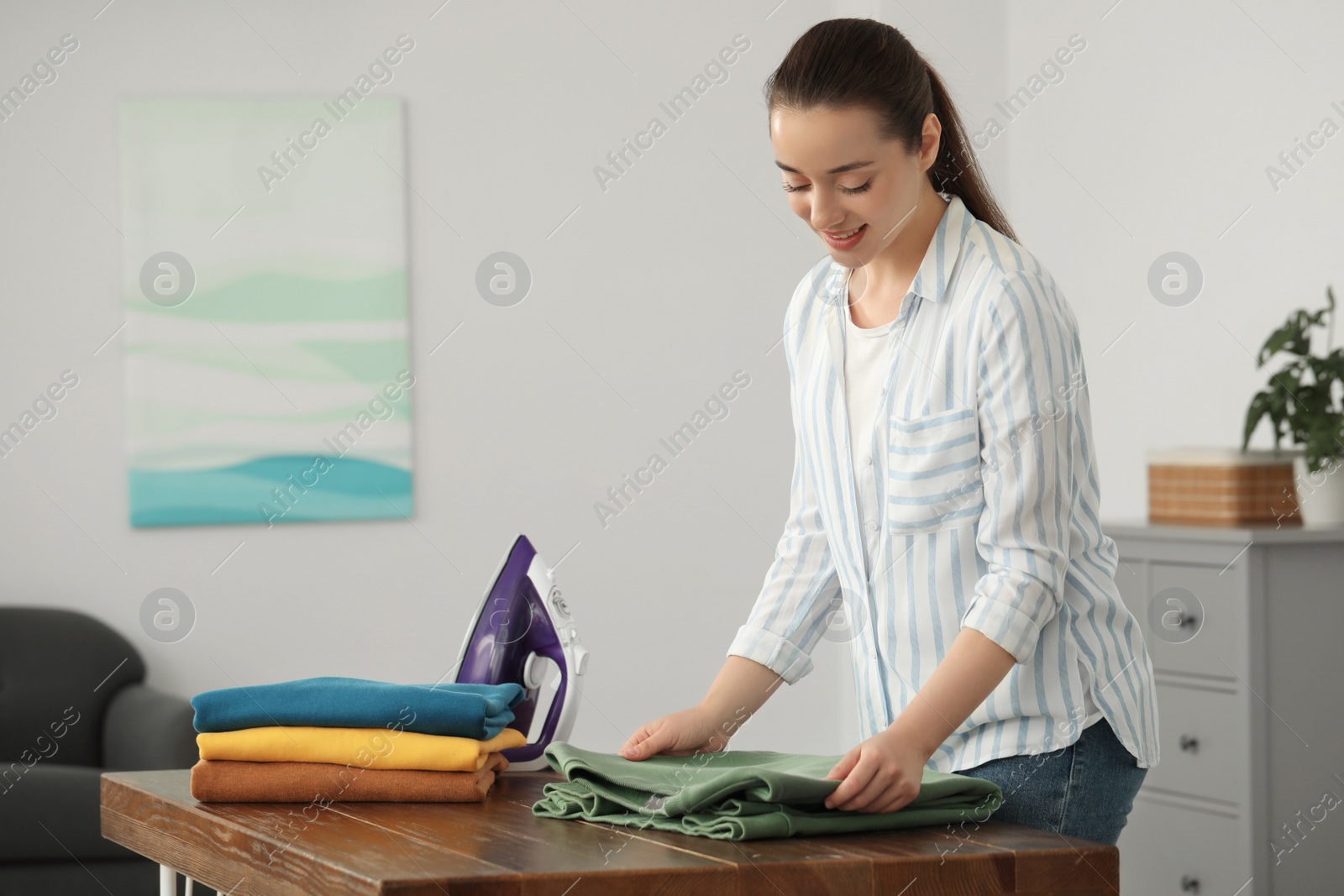 Photo of Young woman folding clothes at wooden table indoors