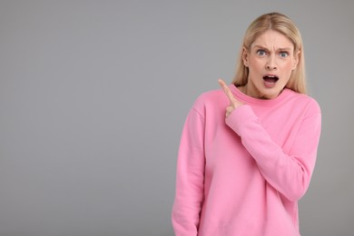 Photo of Surprised woman pointing at something on grey background, space for text