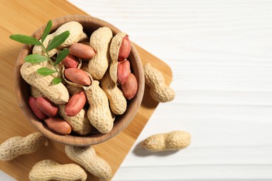 Fresh unpeeled peanuts in bowl and twig on white wooden table, top view. Space for text