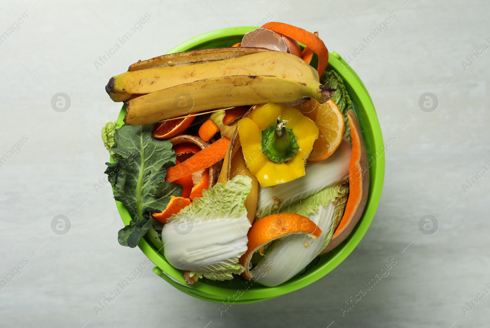 Photo of Trash bin with organic waste for composting on light background, top view