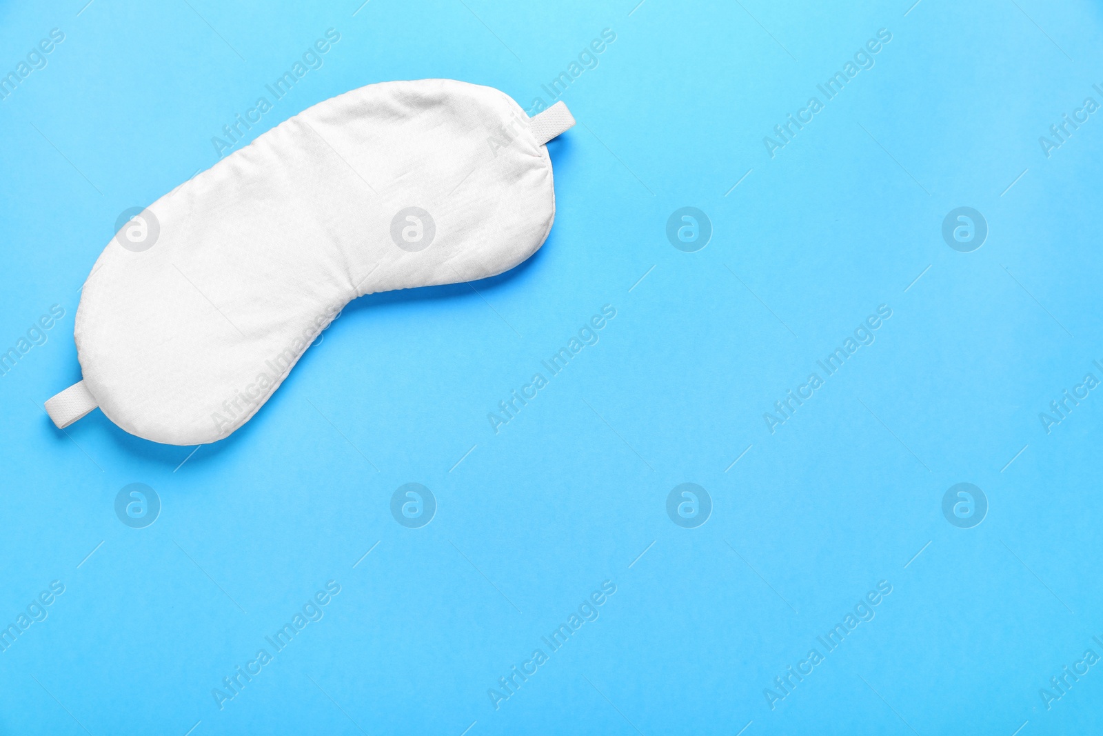 Photo of Soft sleep mask on light blue background, top view. Space for text