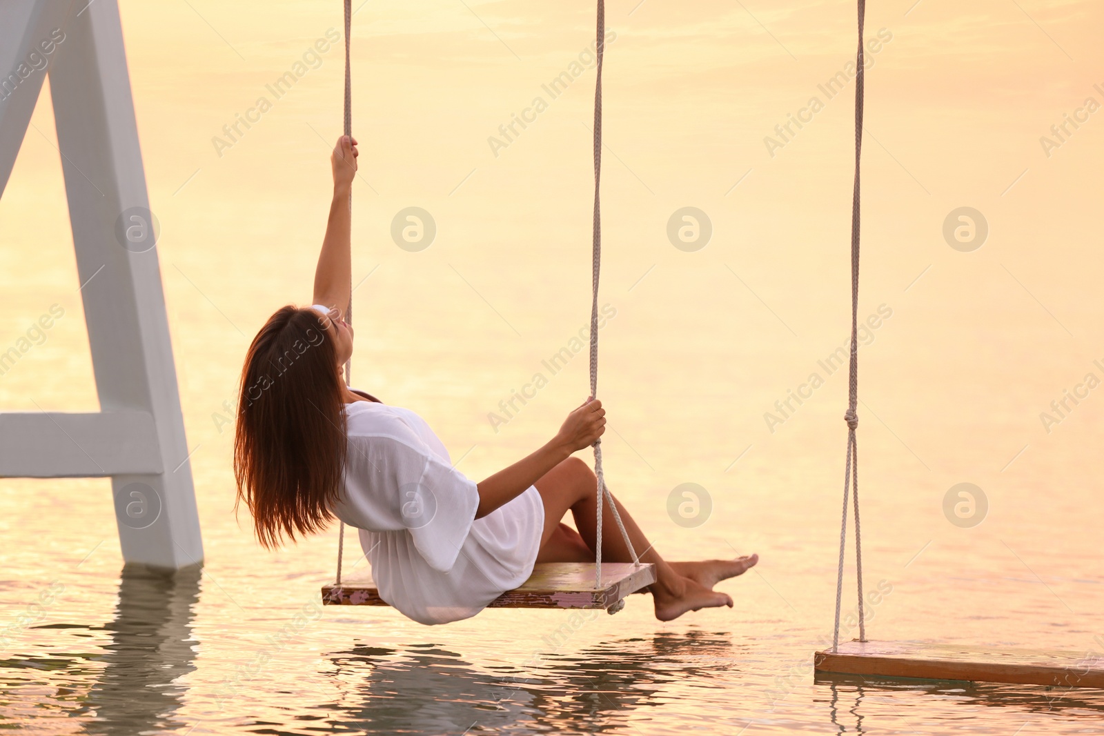 Photo of Young woman enjoying sunrise on swing over water