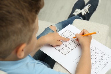 Photo of Little boy solving sudoku puzzle on sofa at home, closeup