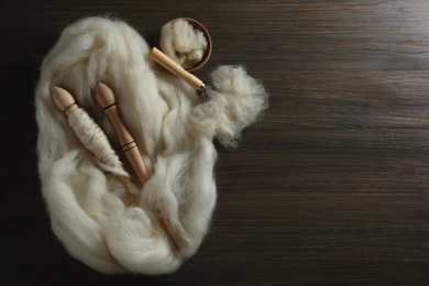 Soft white wool, spindles and comb on wooden table, flat lay. Space for text