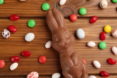 Photo of Flat lay composition with chocolate Easter bunny and candies on wooden table
