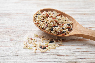 Photo of Mix of different brown rice in spoon on white wooden table, closeup