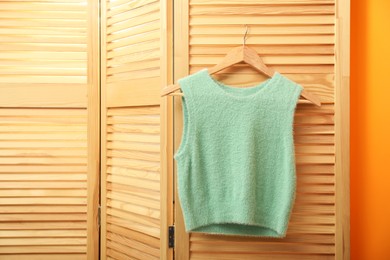 Photo of Stylish sweater vest hanging on wooden folding screen near orange wall, space for text