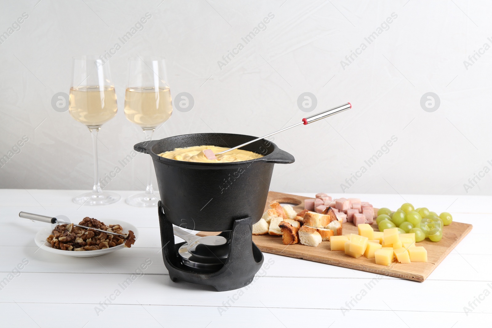 Photo of Fondue pot with tasty melted cheese, forks, wine and different snacks on white wooden table