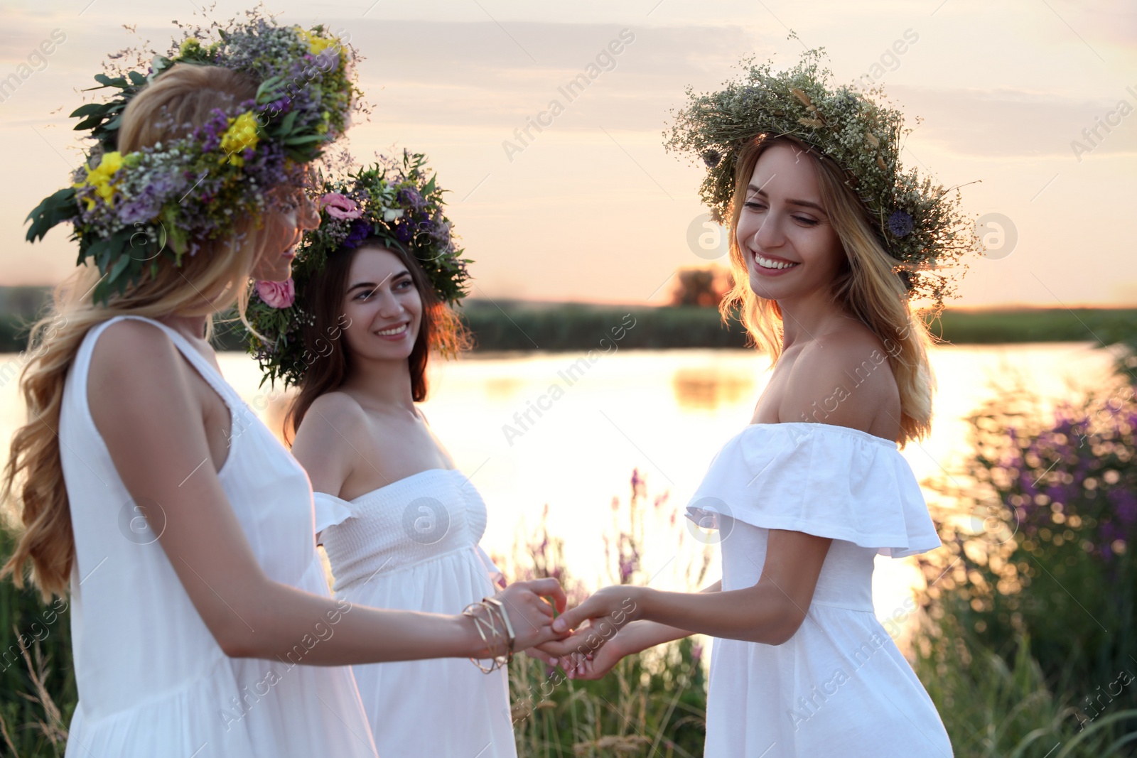 Photo of Young women wearing wreaths made of beautiful flowers outdoors at sunset