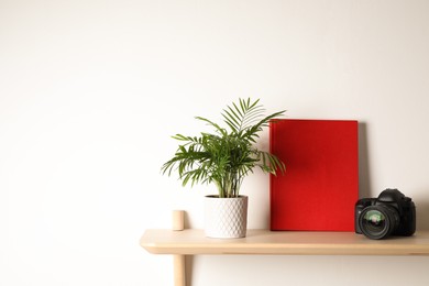 Photo of Book, potted plant and professional camera on wooden shelf indoors, space for text