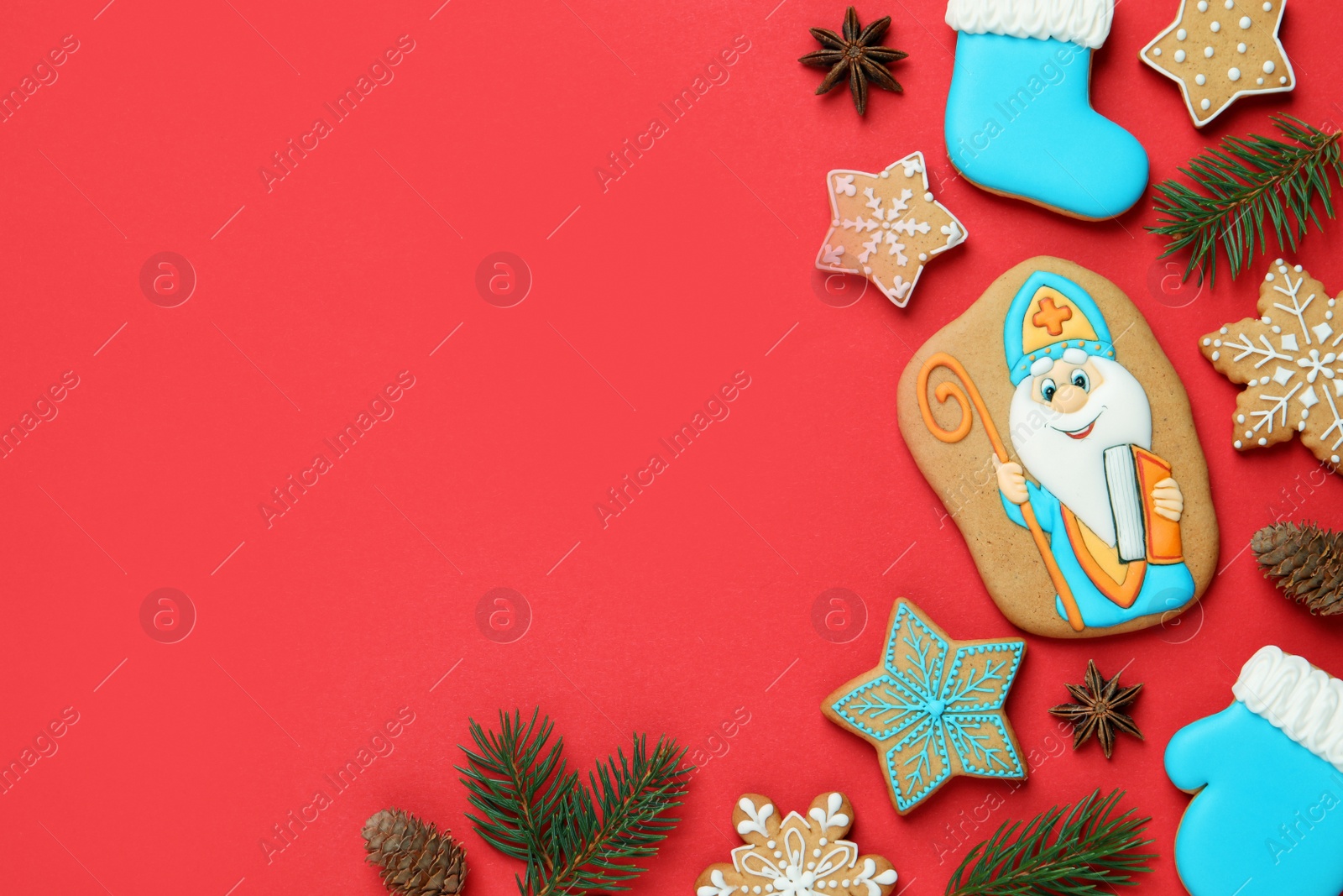 Photo of Tasty gingerbread cookies and fir branches on red background, flat lay with space for text. St. Nicholas Day celebration