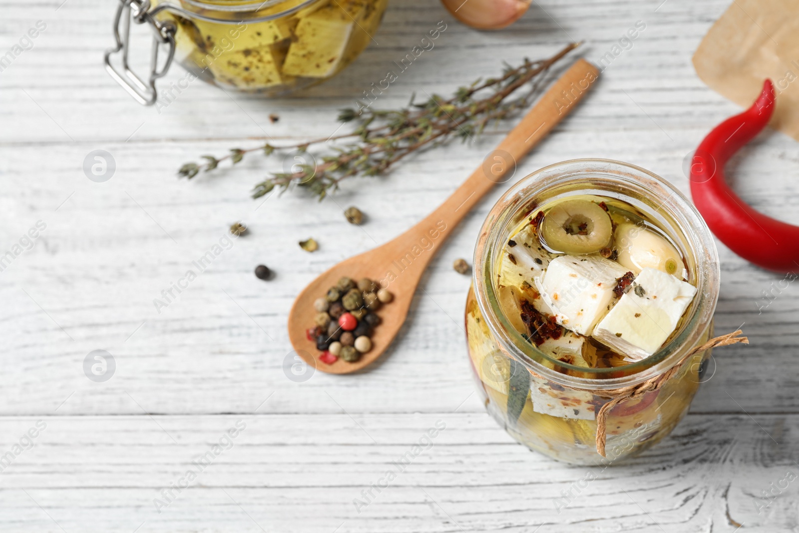 Photo of Jar with feta cheese marinated in oil on white wooden table, above view. Pickled food