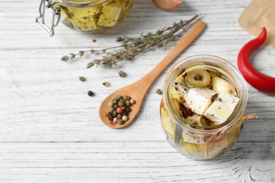 Photo of Jar with feta cheese marinated in oil on white wooden table, above view. Pickled food