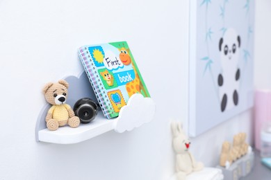 Photo of Small camera hidden between toy bear and book on shelf in baby room