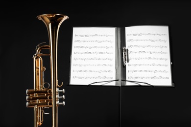 Trumpet and note stand with music sheets on black background