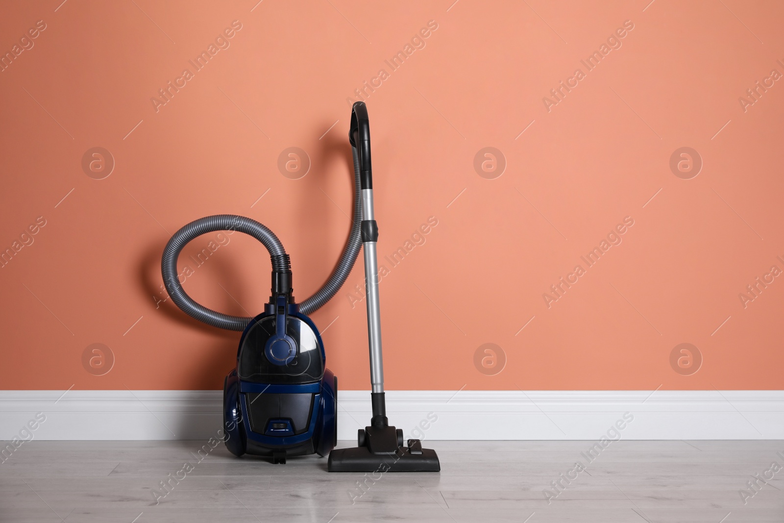 Photo of Modern vacuum cleaner on floor near orange wall indoors. Space for text