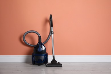 Modern vacuum cleaner on floor near orange wall indoors. Space for text