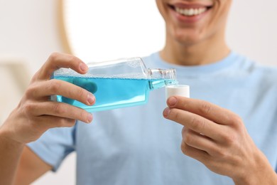 Photo of Young man using mouthwash in bathroom, closeup