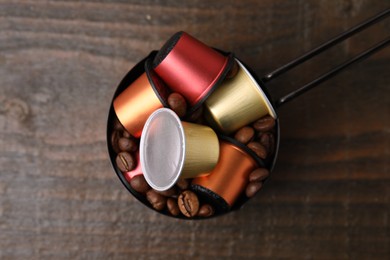 Saucepan with coffee capsules and beans on wooden table, top view