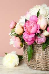 Basket with beautiful peonies on wooden table