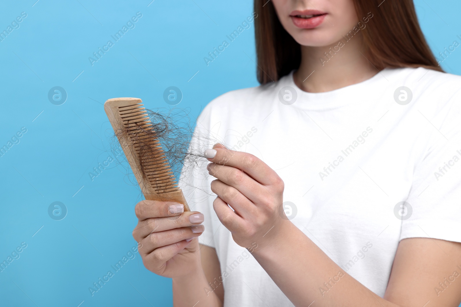 Photo of Woman untangling her lost hair from comb on light blue background, closeup. Alopecia problem