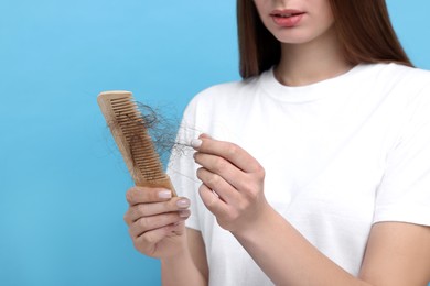 Woman untangling her lost hair from comb on light blue background, closeup. Alopecia problem