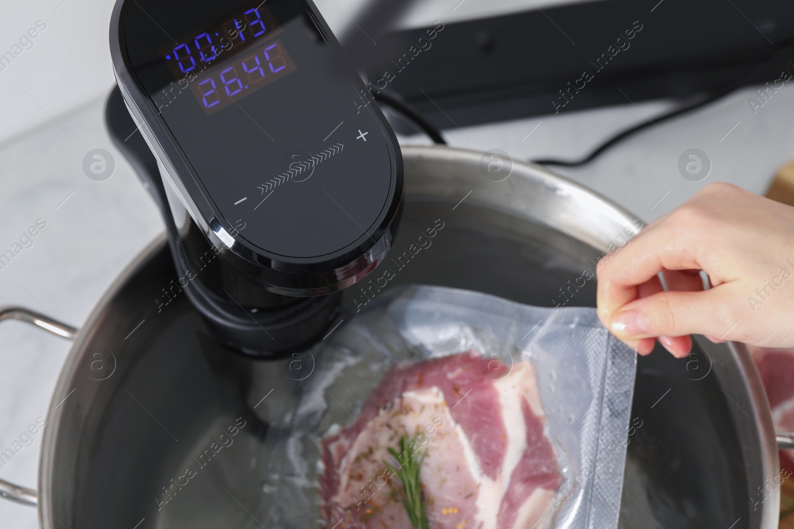 Photo of Woman putting vacuum packed meat into pot with sous vide cooker in kitchen, closeup. Thermal immersion circulator