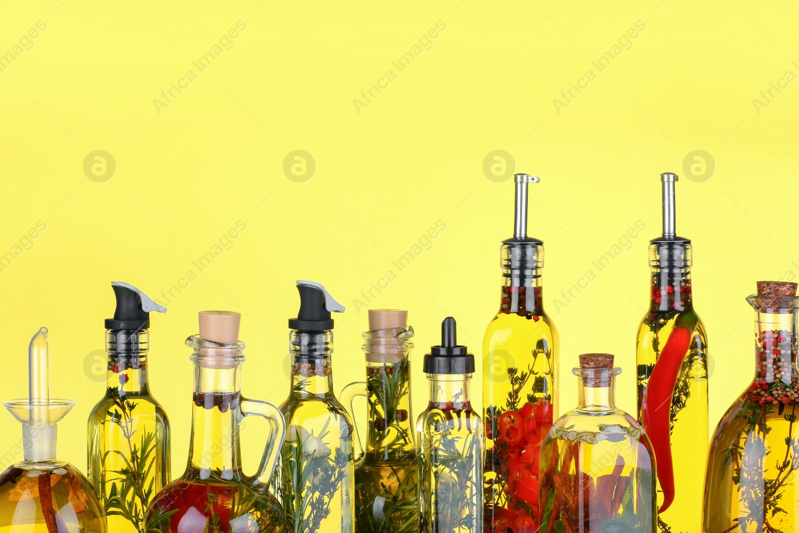 Photo of Cooking oil with different spices and herbs in bottles on yellow background