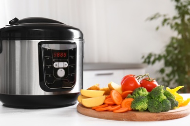Photo of Modern multi cooker and wooden board with vegetables on white table indoors