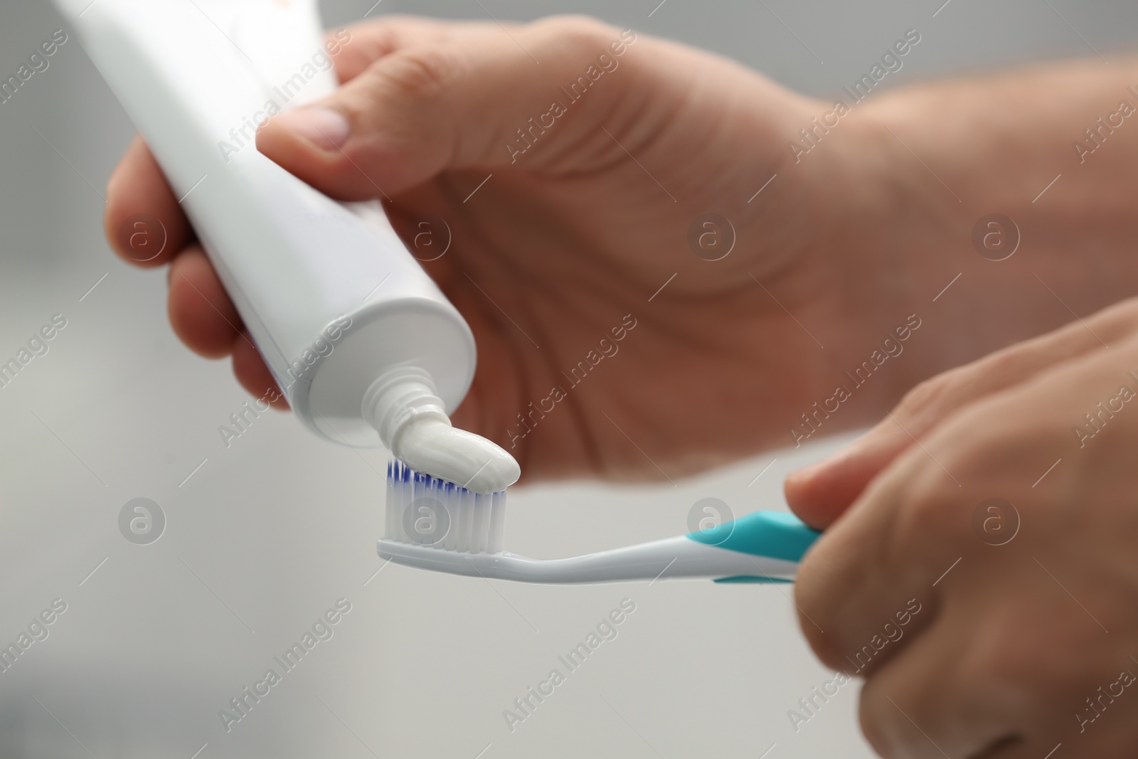 Photo of Man applying toothpaste on brush against blurred background, closeup