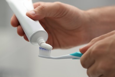 Photo of Man applying toothpaste on brush against blurred background, closeup