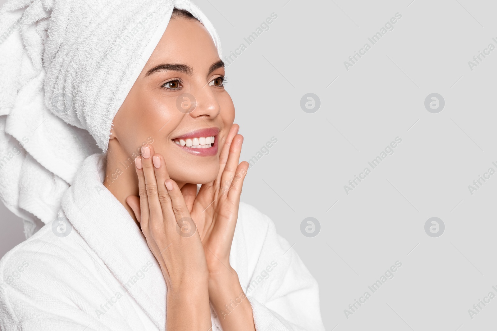 Photo of Young woman in bathrobe with towel on light grey background, space for text. Spa treatment