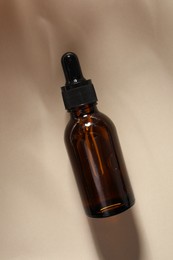 Photo of Bottle of cosmetic serum on beige background, top view