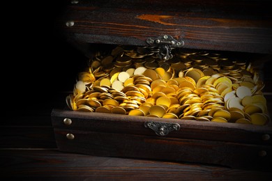 Open treasure chest with gold coins on wooden table, closeup 