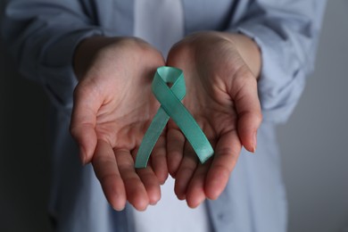 Photo of Woman holding turquoise awareness ribbon on grey background, closeup