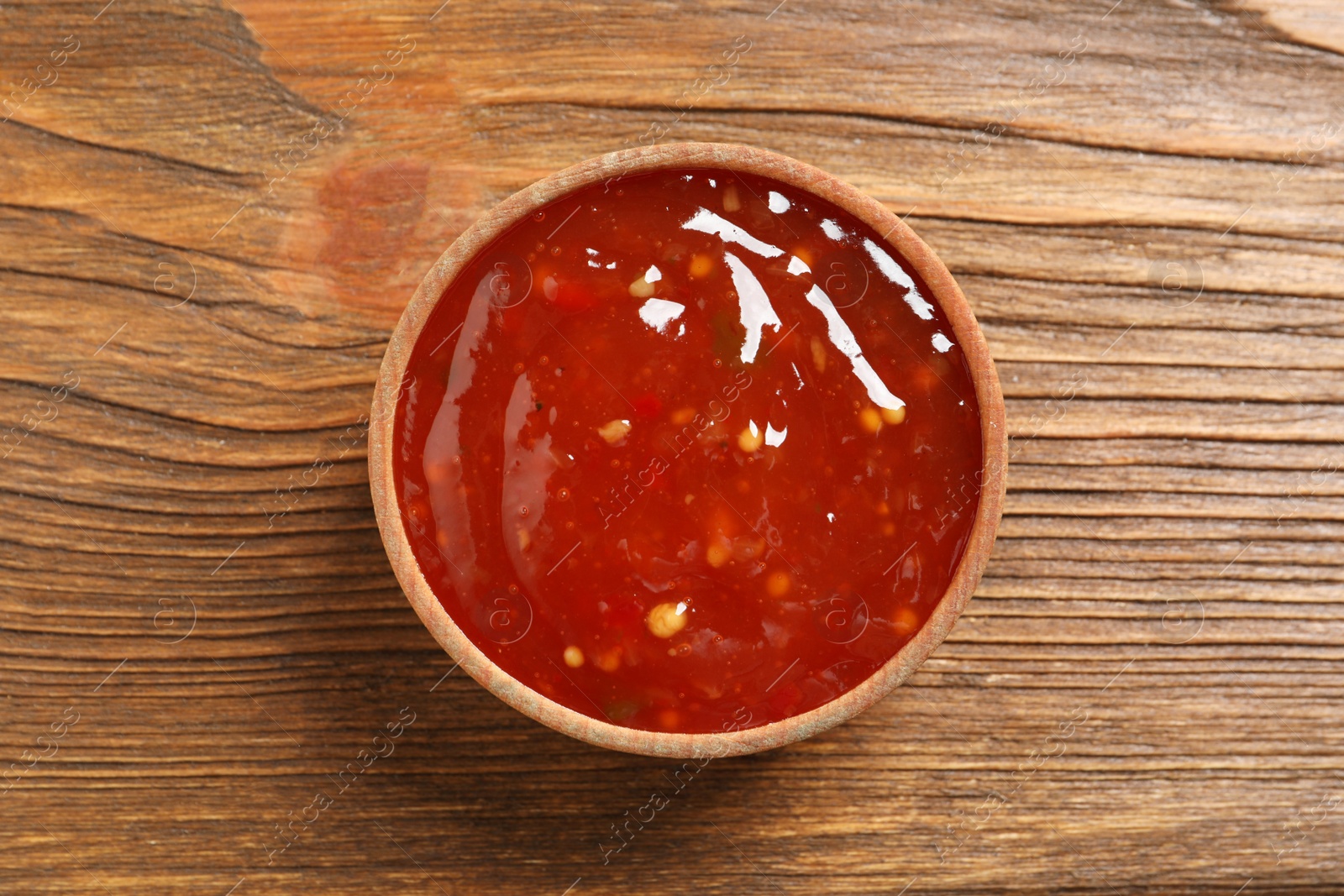 Photo of Spicy chili sauce in bowl on wooden table, top view