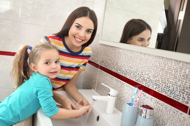 Happy mother and daughter washing hands in bathroom at home