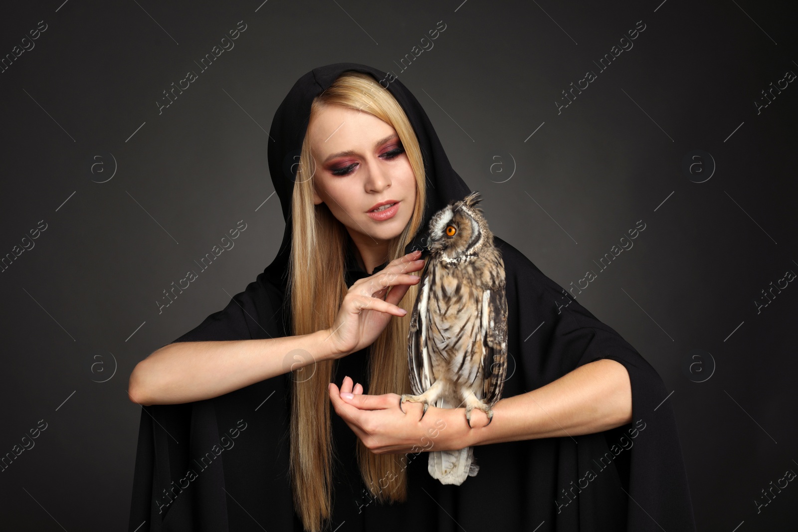 Photo of Witch in black mantle with owl on dark background. Scary fantasy character