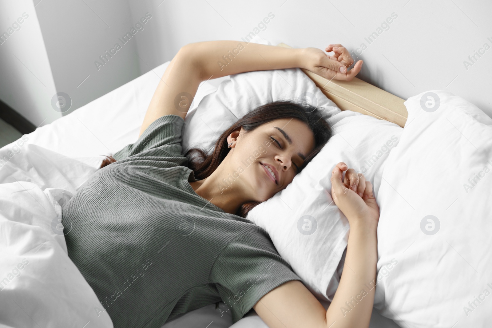 Photo of Happy young woman lying on soft pillow in bed at home