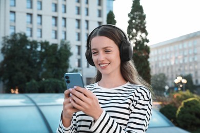 Smiling woman in headphones using smartphone on city street