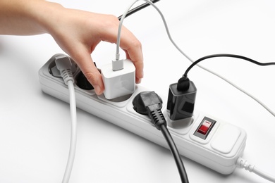 Woman inserting power plug into extension cord on white background, closeup. Electrician's professional equipment