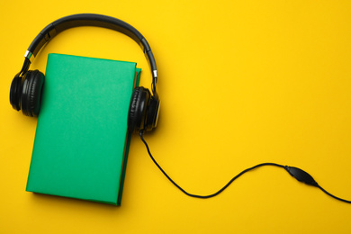 Book and modern headphones on yellow background, flat lay. Space for text