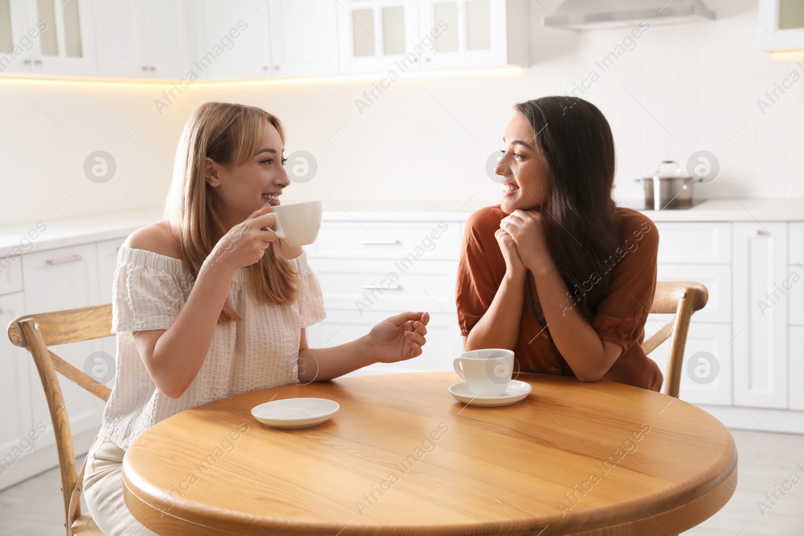 Photo of Young women talking while drinking tea at table in kitchen