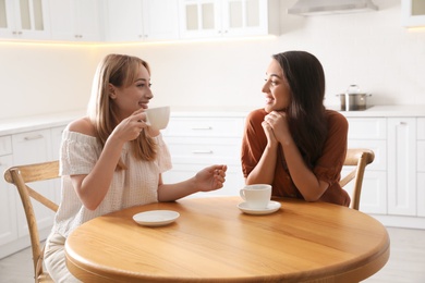 Young women talking while drinking tea at table in kitchen