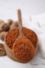 Bowl and spoon with nutmeg powder on white table, closeup